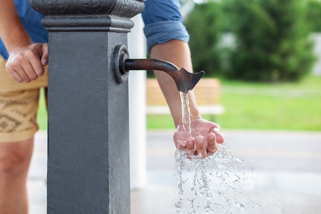 Hombre lavándose las manos en el grifo de agua con agua en el parque. Columna para beber