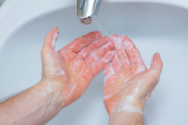 Hombre lavarse las manos con jabón debajo del lavabo del baño.