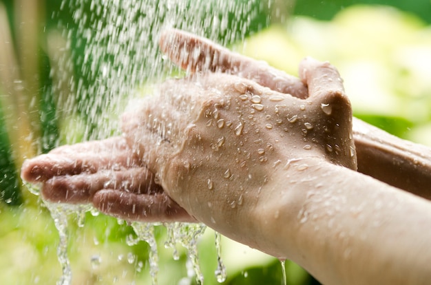 Hombre lave las manos bajo el chapoteo del agua en la naturaleza.