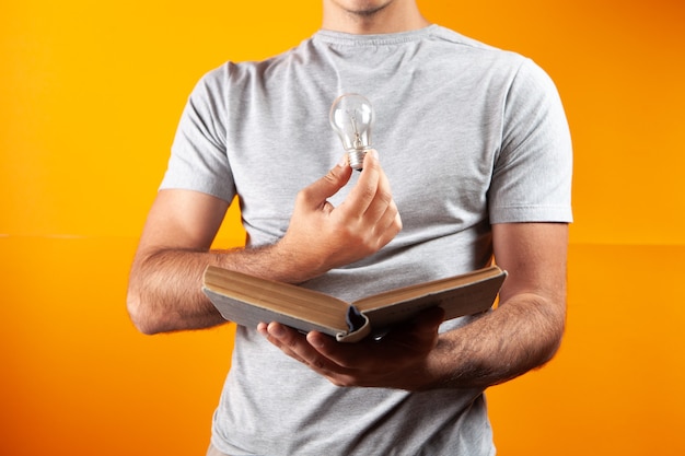 Un hombre lee un libro y sostiene una bombilla. idea conceptual del libro sobre la oficina naranja