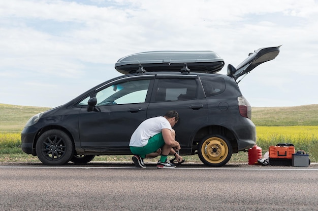 Un hombre levanta un automóvil para reemplazar un neumático después de un pinchazo al costado de la carretera usando un gato hidráulico insertado debajo del cuerpo levanta el automóvil y coloca una rueda de repuesto