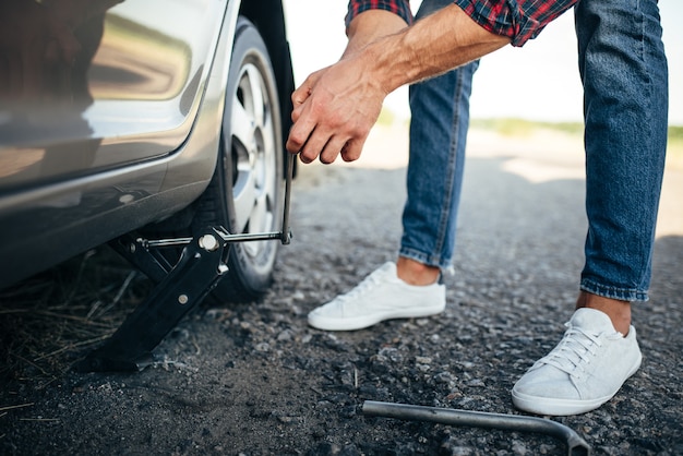 Foto hombre levanta coche roto, reemplazo de rueda