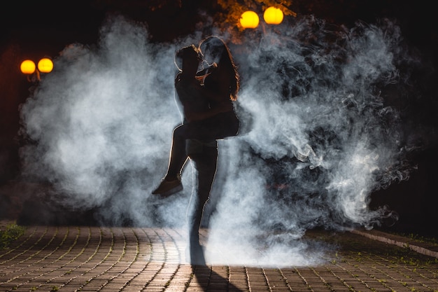 El hombre levantando a una mujer en la calle con un humo. Noche