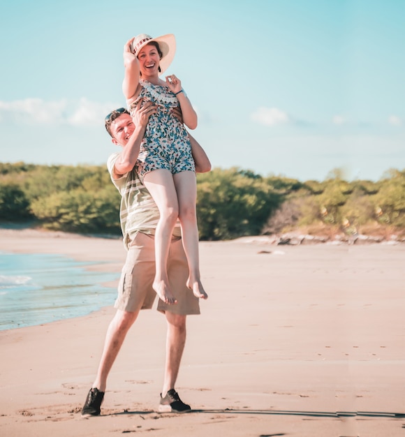 Hombre levantando a mujer en la playa en el aire, hombre sonriendo feliz con una mujer en la playa, estilo de vida de hombre y mujer felices en la playa