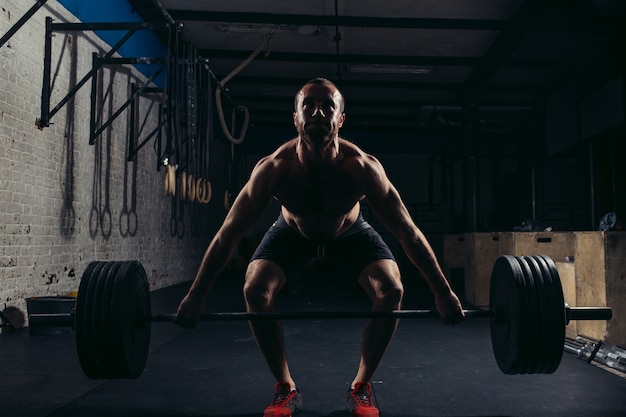 Hombre levantando pesas. Entrenamiento de hombre musculoso en el gimnasio haciendo ejercicios con barra