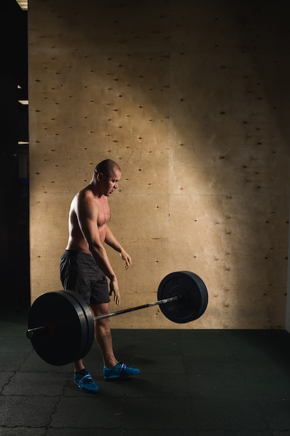 Hombre levantando pesas. Entrenamiento de hombre musculoso en el gimnasio haciendo ejercicios con barra