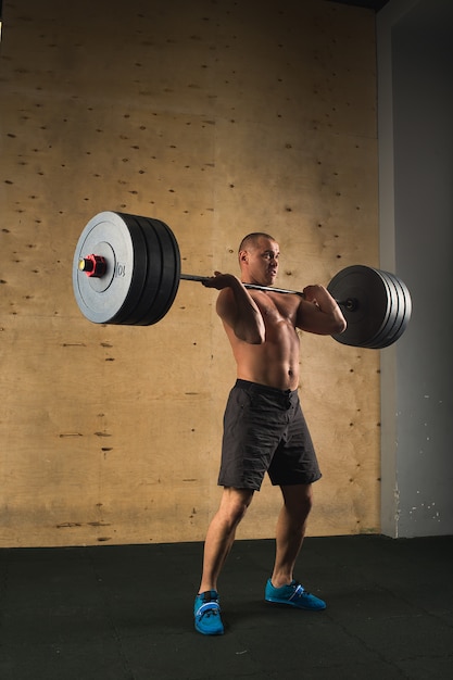 Hombre levantando pesas. Entrenamiento de hombre musculoso en el gimnasio haciendo ejercicios con barra