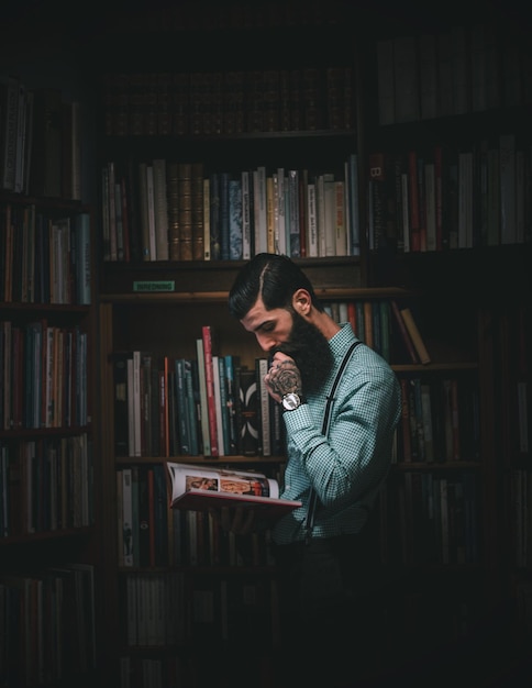 Hombre leyendo un libro mientras está de pie contra los estantes