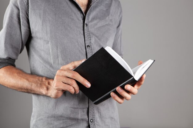 Hombre leyendo un libro mientras está de pie sobre fondo gris