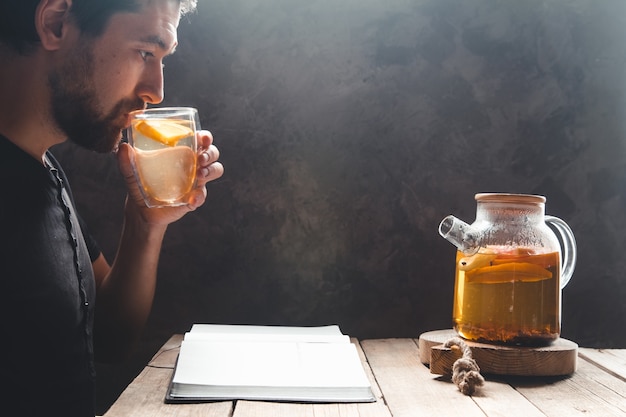 Un hombre leyendo un libro con té cítrico. Educación, bebida saludable, formación.