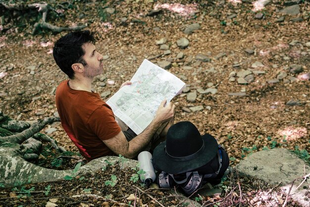 Foto hombre leyendo un mapa mientras está sentado en el bosque