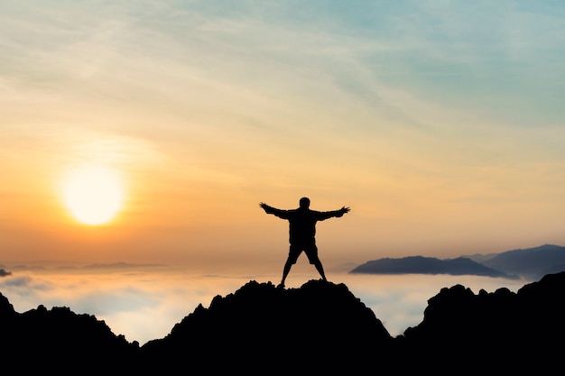 Hombre de la libertad con la silueta de brazos abiertos en la salida del sol en el fondo de la niebla del cielo de la montaña superior