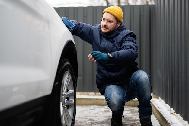 El hombre limpia el automóvil SUV americano con un paño de microfibra después de lavarlo en clima frío