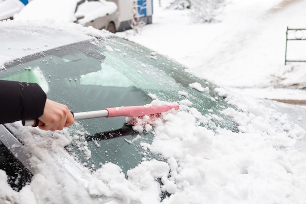 El hombre limpia el coche de la nieve con un cepillo