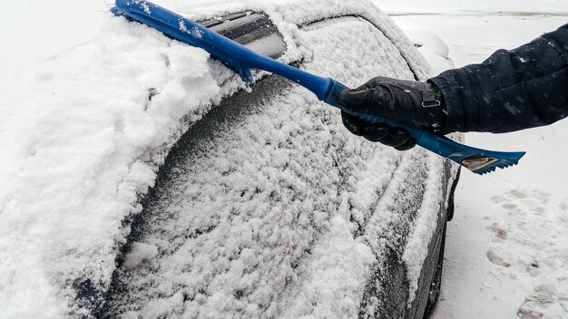 El hombre limpia el coche de la nieve con un cepillo