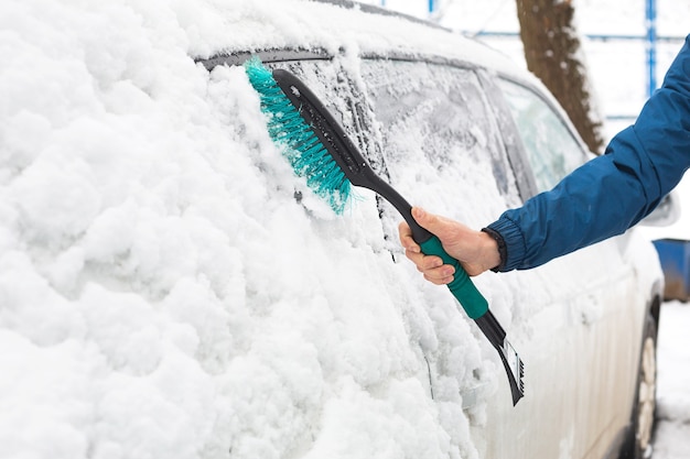 Un hombre limpia la nieve de un automóvil después de una nevada.