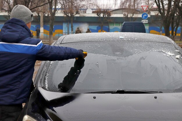 Un hombre limpia el parabrisas de un coche con un raspador