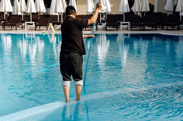 Un hombre limpia la piscina Hombre limpiando la piscina con aspiradora