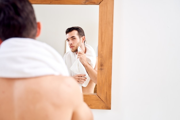 El hombre limpia su toalla mientras está de pie junto al espejo en el baño en la mañana