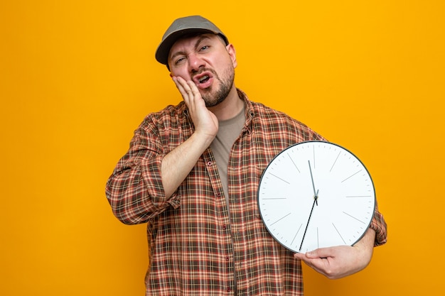 Hombre limpiador eslavo disgustado sosteniendo el reloj y poniendo la mano en la cara