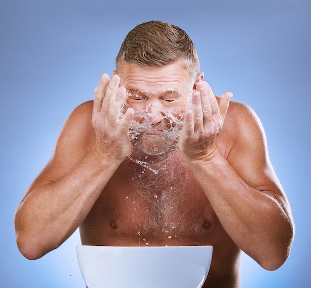 Foto hombre limpiando la cara, las manos y las salpicaduras de agua, higiene y aseo con un rostro limpio sobre fondo azul lavabo de piel masculino mayor y rutina matutina con cuidado cosmético natural y dermatología