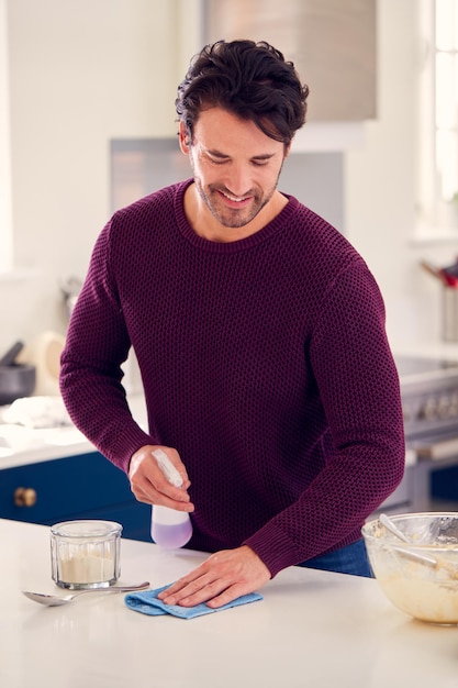 Hombre Limpiando Mostrador De Cocina Con Aerosol Y Paño Después De Hornear Pastel