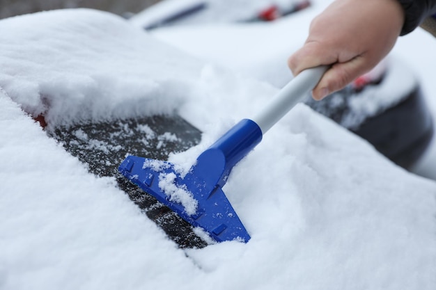 Hombre limpiando la nieve del coche al aire libre en el primer día de invierno