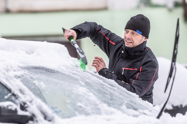 Hombre limpiando la nieve de su coche aparcado fuera tras las fuertes nevadas por la noche.