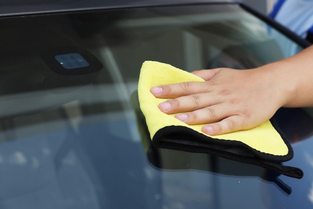 Hombre limpiando el parabrisas del coche con un primer plano de trapo amarillo