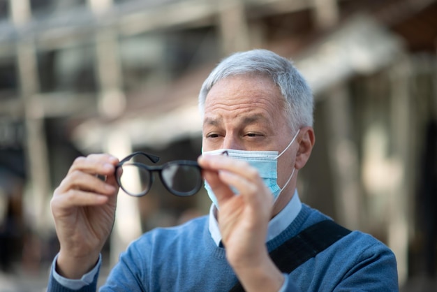 Hombre limpiando sus anteojos empañados debido al concepto de visión de máscara covid coronavirus