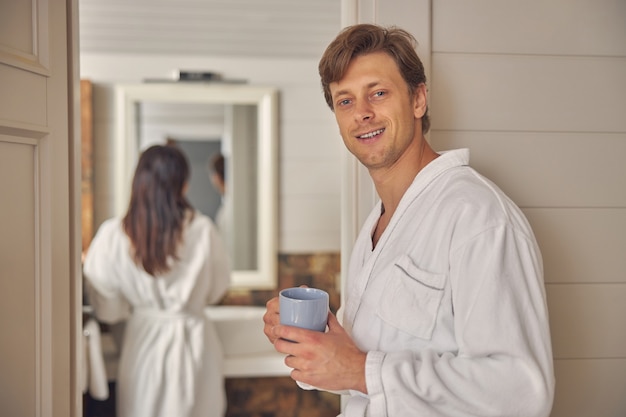 Hombre lindo en bata de baño suave blanca posando y mirando a la cámara de fotos