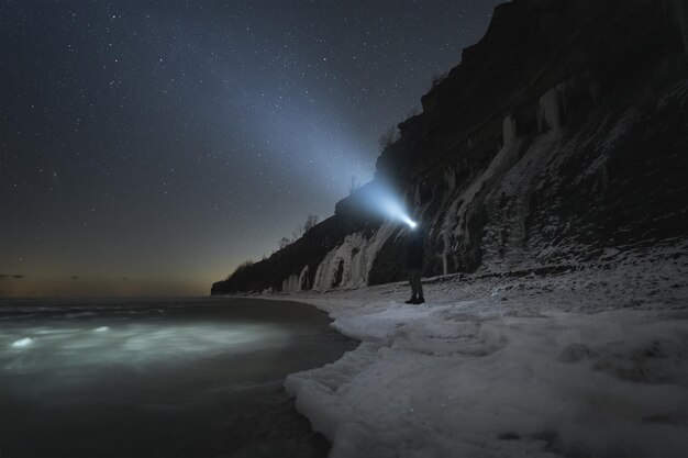 Foto un hombre con una linterna en la empinada costa del mar báltico en paldiski por la noche en invierno