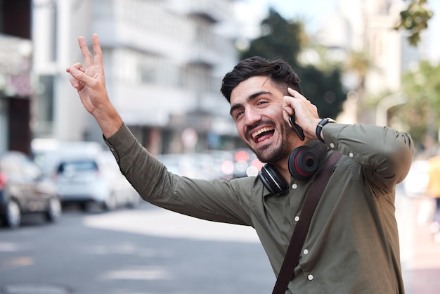 Hombre llama por teléfono y saluda a la ciudad de taxis y sonríe por emoji de lenguaje de señas de paz o cara graciosa en la acera Teléfono inteligente joven empresario y calle para detener el transporte en autobús y el conductor para viajar
