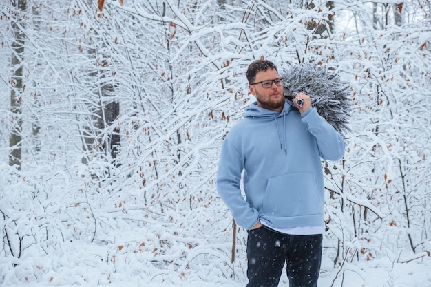 Un hombre lleva un árbol de Navidad cubierto de nieve a través de un bosque de invierno