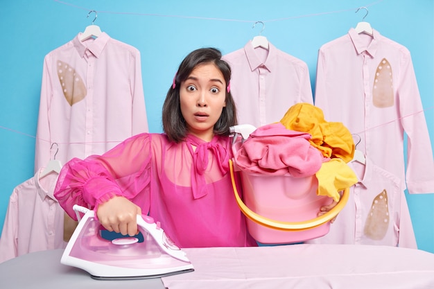 El hombre lleva un balde lleno de ropa lavada utiliza poses de plancha de vapor eléctrica cerca de la tabla de planchar tiene muchas responsabilidades