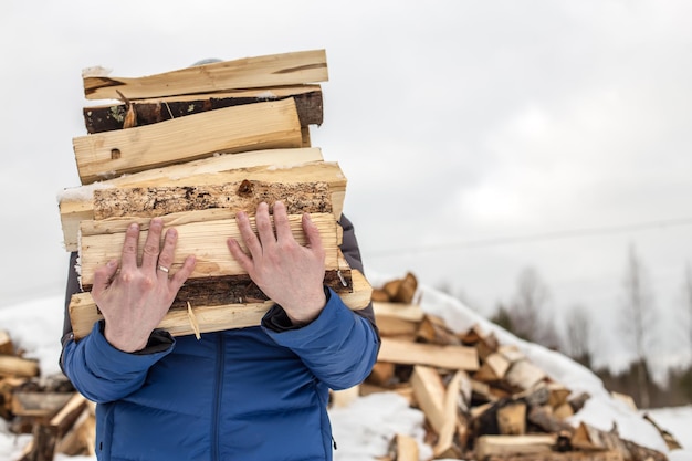 El hombre lleva leña picada en invierno en la aldea contra montones de otra madera cubiertos de nieve