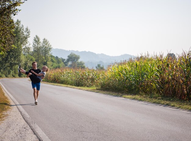 el hombre lleva a una mujer en sus brazos mientras trota por un camino rural, el ejercicio y el concepto de fitness