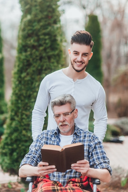 Un hombre lleva a su padre, se divierten y se ríen mientras leen un libro.