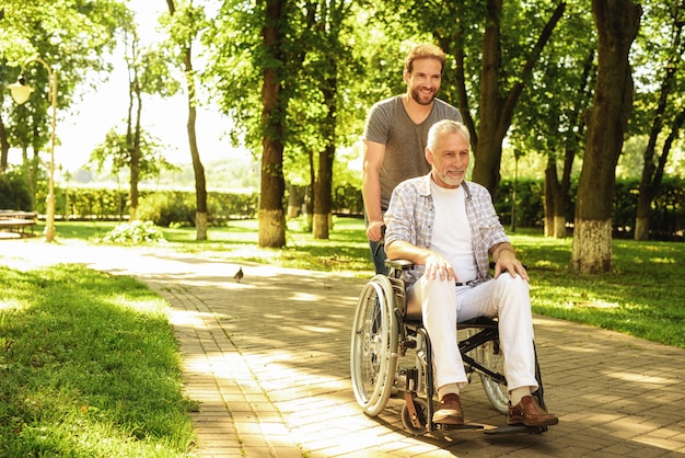 El hombre lleva a su sonriente padre en una silla de ruedas.