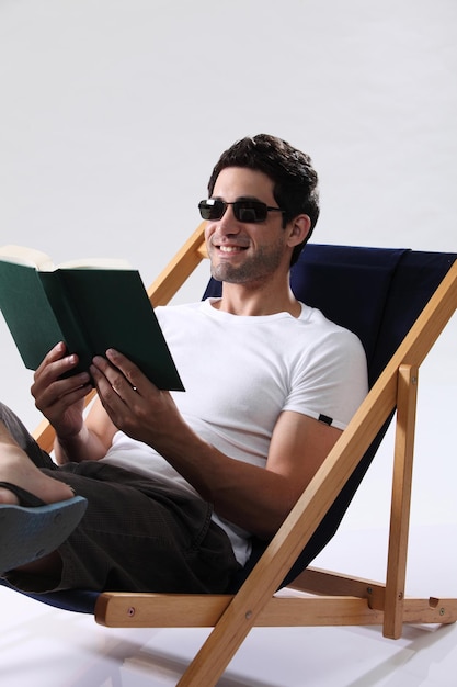 hombre, llevando gafas de sol, tenencia, libro, acostado, en, tumbona