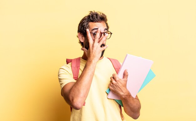 Hombre loco expresivo que parece sorprendido, asustado o aterrorizado, cubriendo la cara con la mano. concepto de estudiante adulto