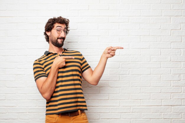 Hombre loco o tonto joven que gesticula y que expresa emociones contra fondo de la pared de ladrillo