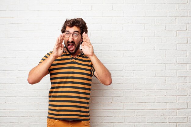 Hombre loco o tonto joven que gesticula y que expresa emociones contra fondo de la pared de ladrillo