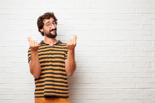 Hombre loco o tonto joven que gesticula y que expresa emociones contra fondo de la pared de ladrillo