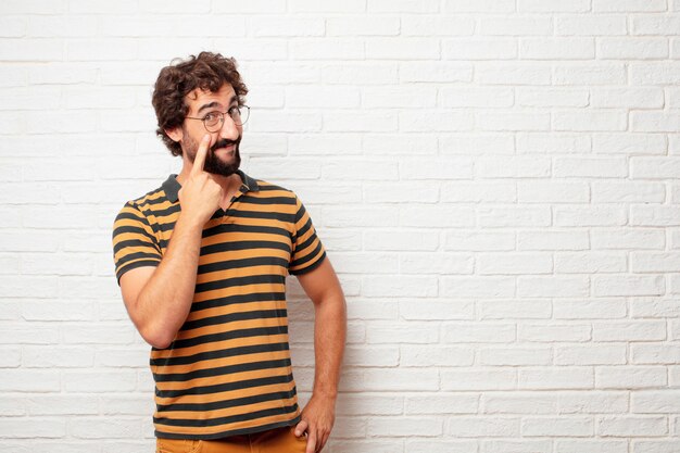 Hombre loco o tonto joven que gesticula y que expresa emociones contra fondo de la pared de ladrillo