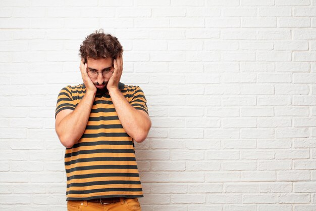 Foto hombre loco o tonto joven que gesticula y que expresa emociones contra fondo de la pared de ladrillo