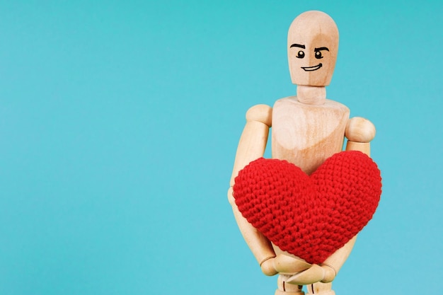 Hombre de madera con corazón rojo sobre fondo azul.