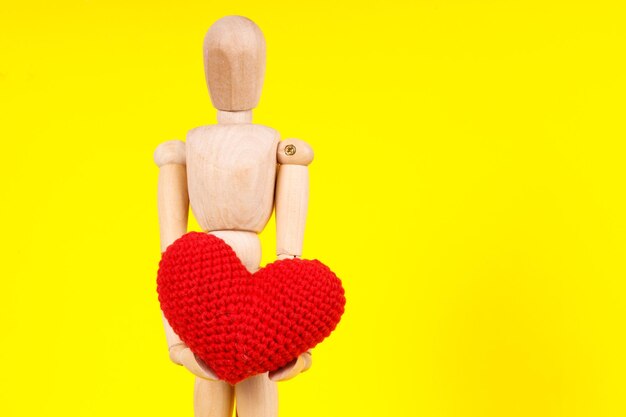 Hombre de madera con un corazón rojo en sus manos sobre un fondo amarillo Foto de alta calidad