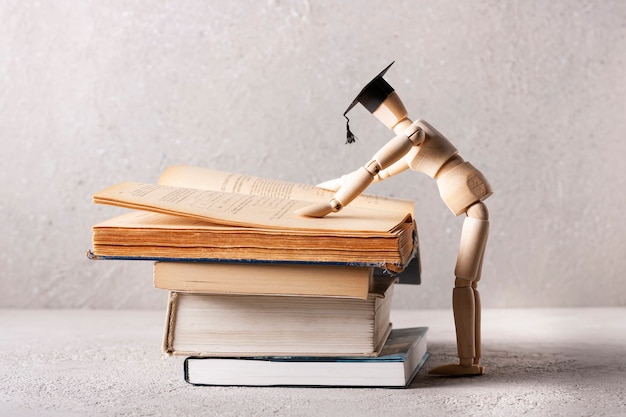 Un hombre de madera con un sombrero de estudiante lee un libro de texto