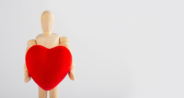 Hombre de madera sosteniendo una figurilla de corazón en sus manos sobre un blanco